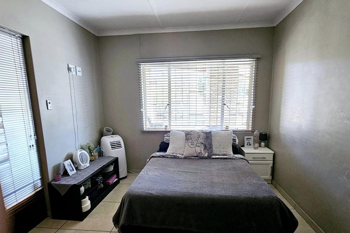 A functional bedroom featuring tiled flooring, dual window treatments with fitted blinds, and neutral wall finishes.