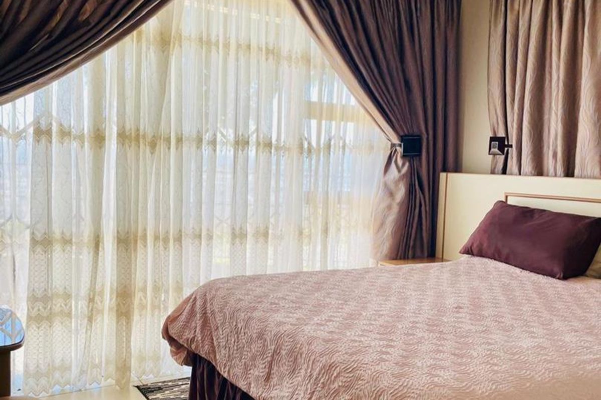 A bedroom featuring tiled flooring, a ceiling light fixture, and a large sliding glass door with curtains providing natural light.