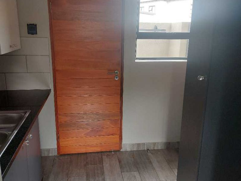A functional scullery area featuring built-in cabinetry, a stainless steel sink, tiled flooring, and a wooden door leading to the exterior.