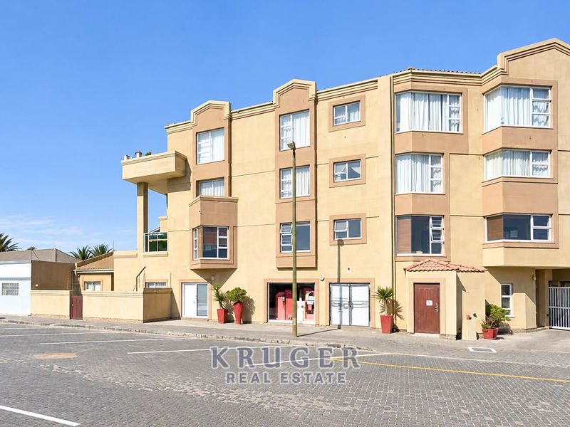 Front elevation of the Toscana apartment complex, featuring a multi-story facade with bay windows, a paved parking area, and secure gated access.