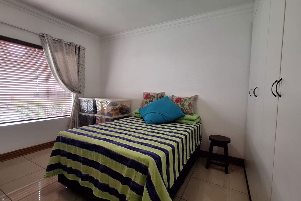 A functional bedroom featuring tiled flooring, built-in cupboards, and venetian blinds, offering a clean and neutral space.