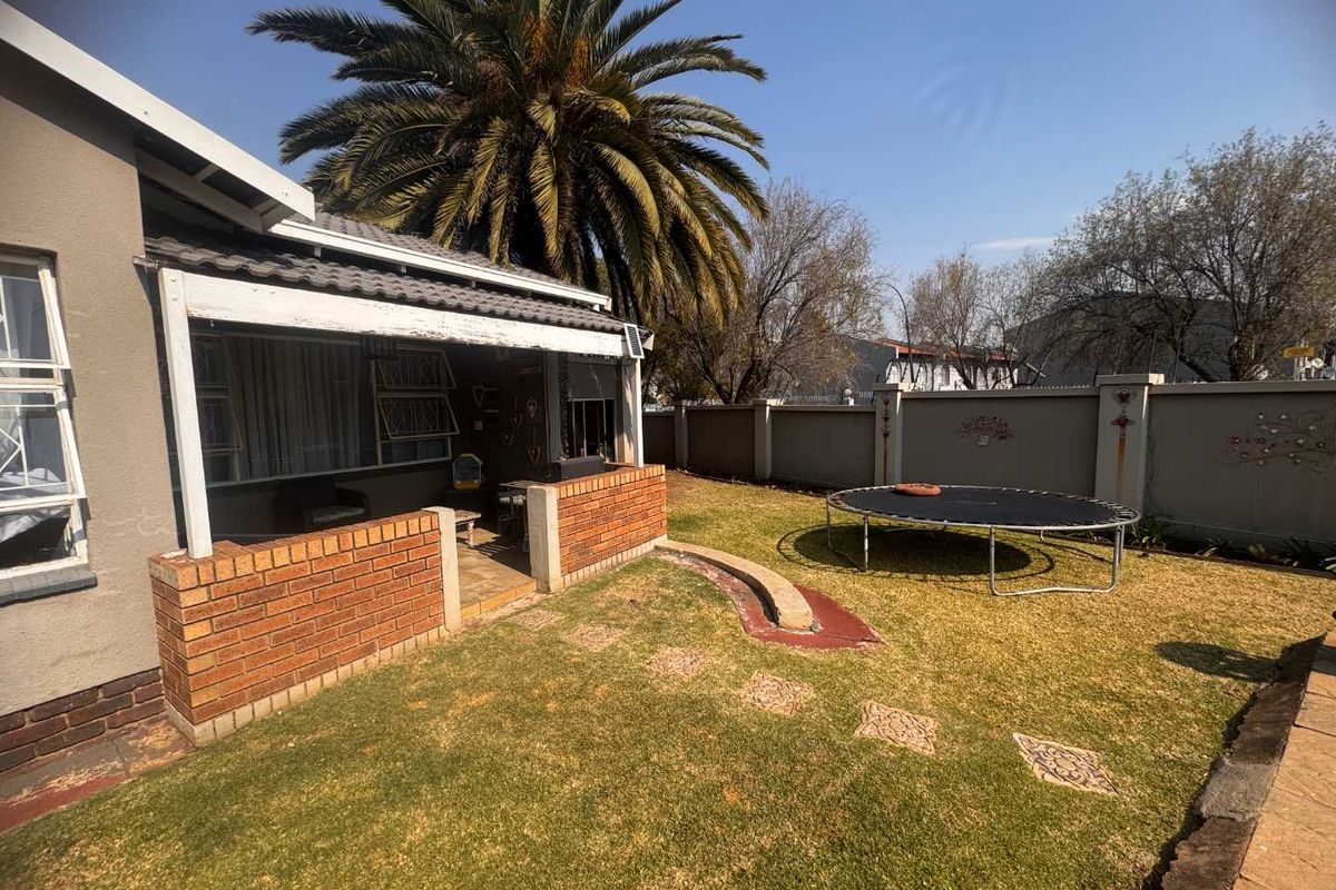 Rear garden view featuring a covered patio with brick walling, a lawn area, and perimeter boundary walls.