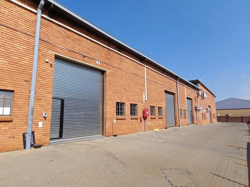 Exterior view of an industrial warehouse facility featuring face-brick facade, multiple roller shutter doors, and paved driveway access.