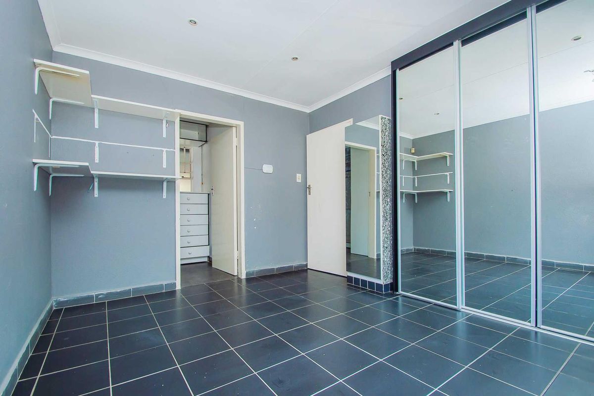 A bedroom featuring dark tiled flooring, built-in mirrored sliding wardrobes, and wall-mounted shelving, with an adjoining walk-in closet area.