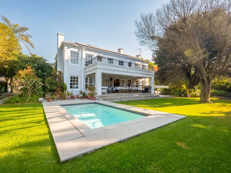 Rear view of a two-story residence featuring a swimming pool, stone-paved patio, and an upper-level balcony with wrought iron railings.