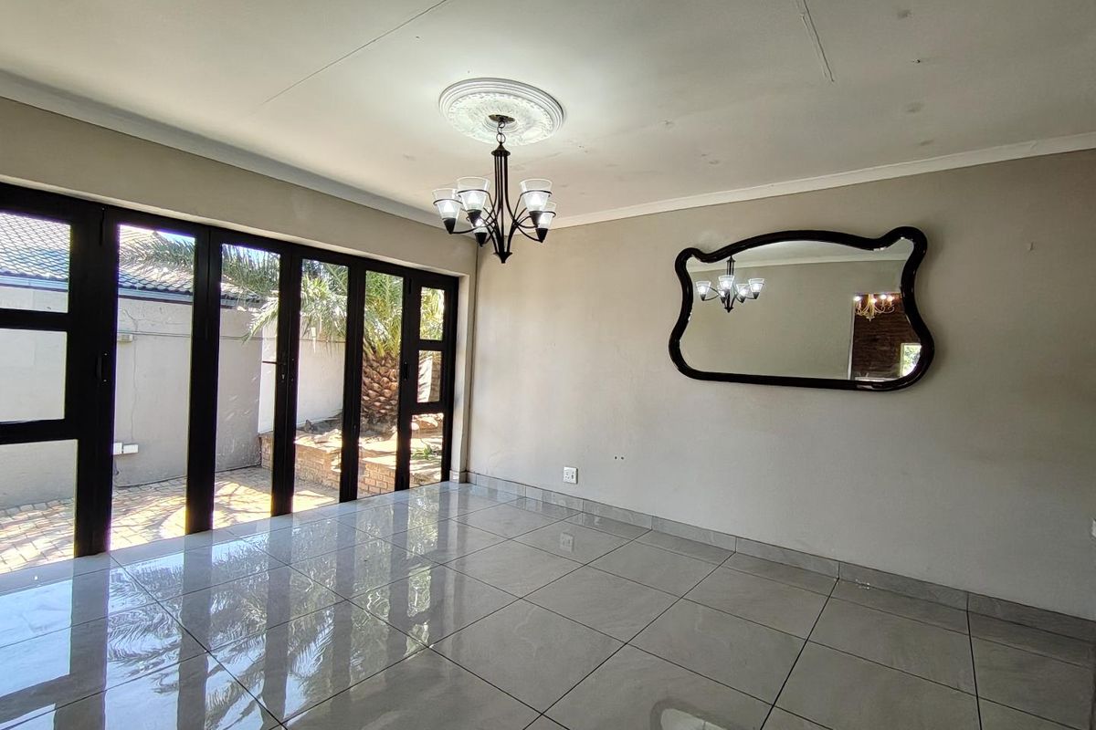 Bright living area featuring large black-framed glass sliding doors leading to an outdoor patio, tiled flooring, and a decorative ceiling rose.