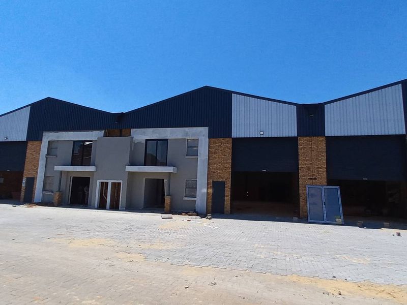Front elevation of an industrial warehouse complex featuring multiple roller shutter doors, brick and plaster finishes, and a paved yard area under construction.