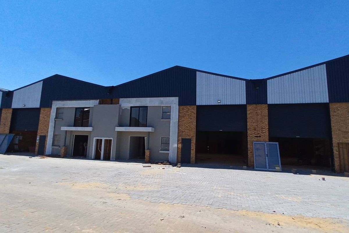 Front elevation of an industrial warehouse complex featuring multiple roller shutter doors, brick and plaster finishes, and a paved yard area under construction.