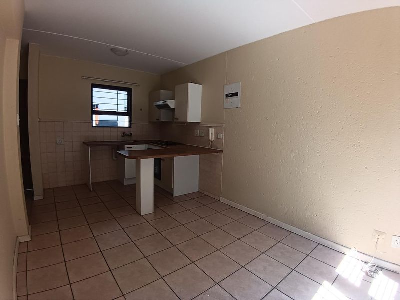 A functional, empty kitchen featuring tiled flooring, built-in cabinetry with laminate countertops, and a tiled splashback, ready for modernization.