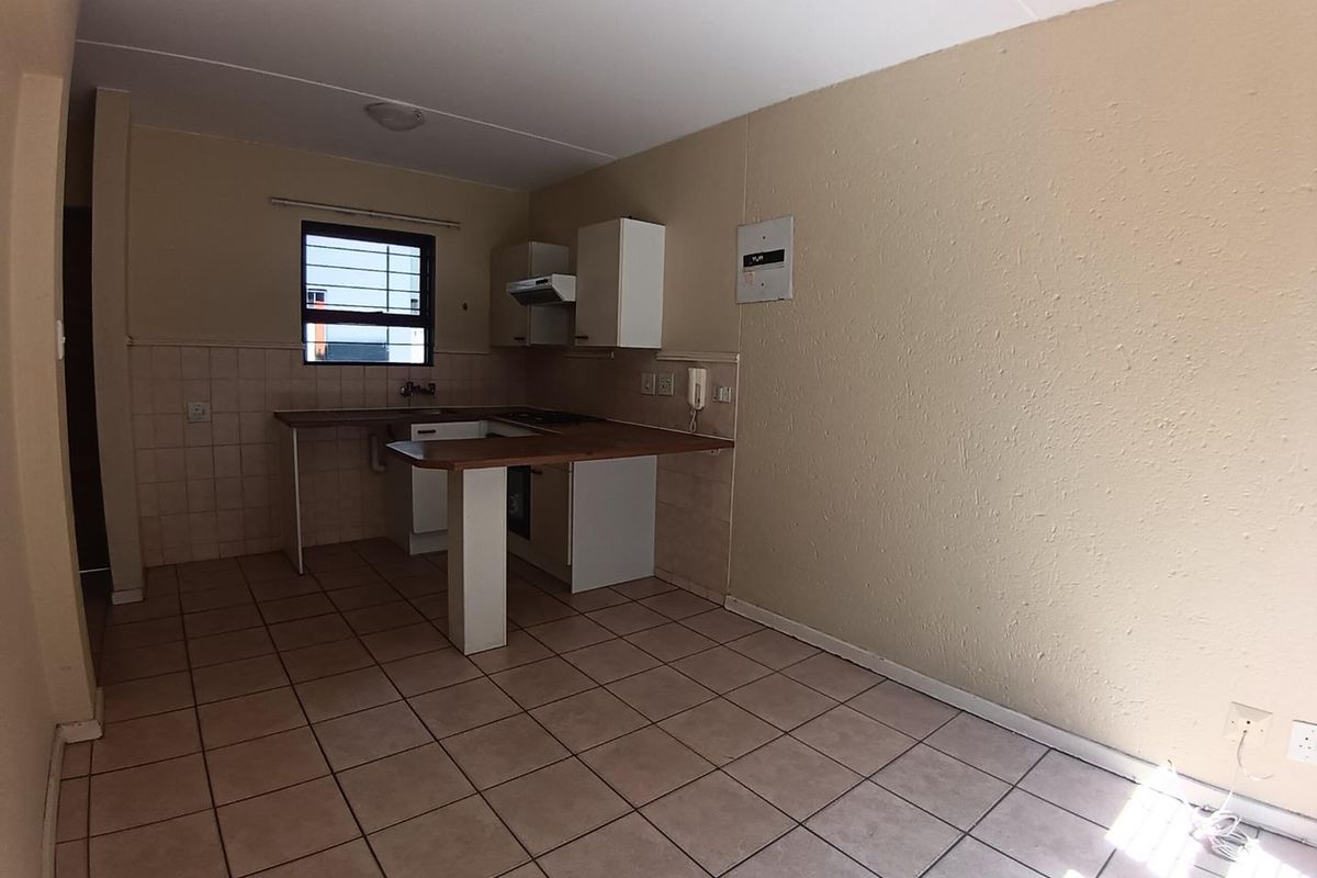 A functional, empty kitchen featuring tiled flooring, built-in cabinetry with laminate countertops, and a tiled splashback, ready for modernization.