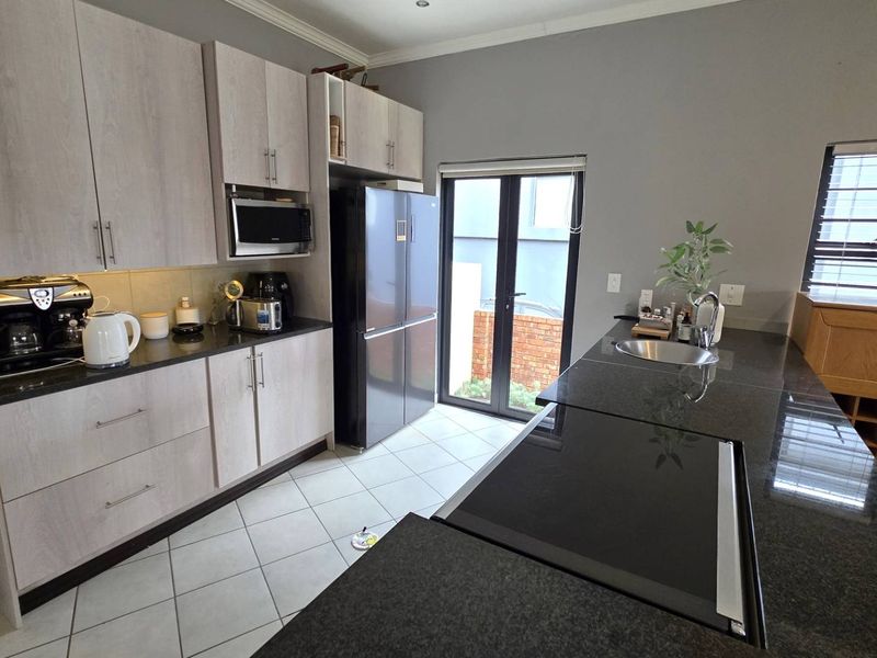 Modern kitchen featuring light wood-grain cabinetry, dark granite countertops, a built-in hob, and direct access to the exterior via glass french doors.