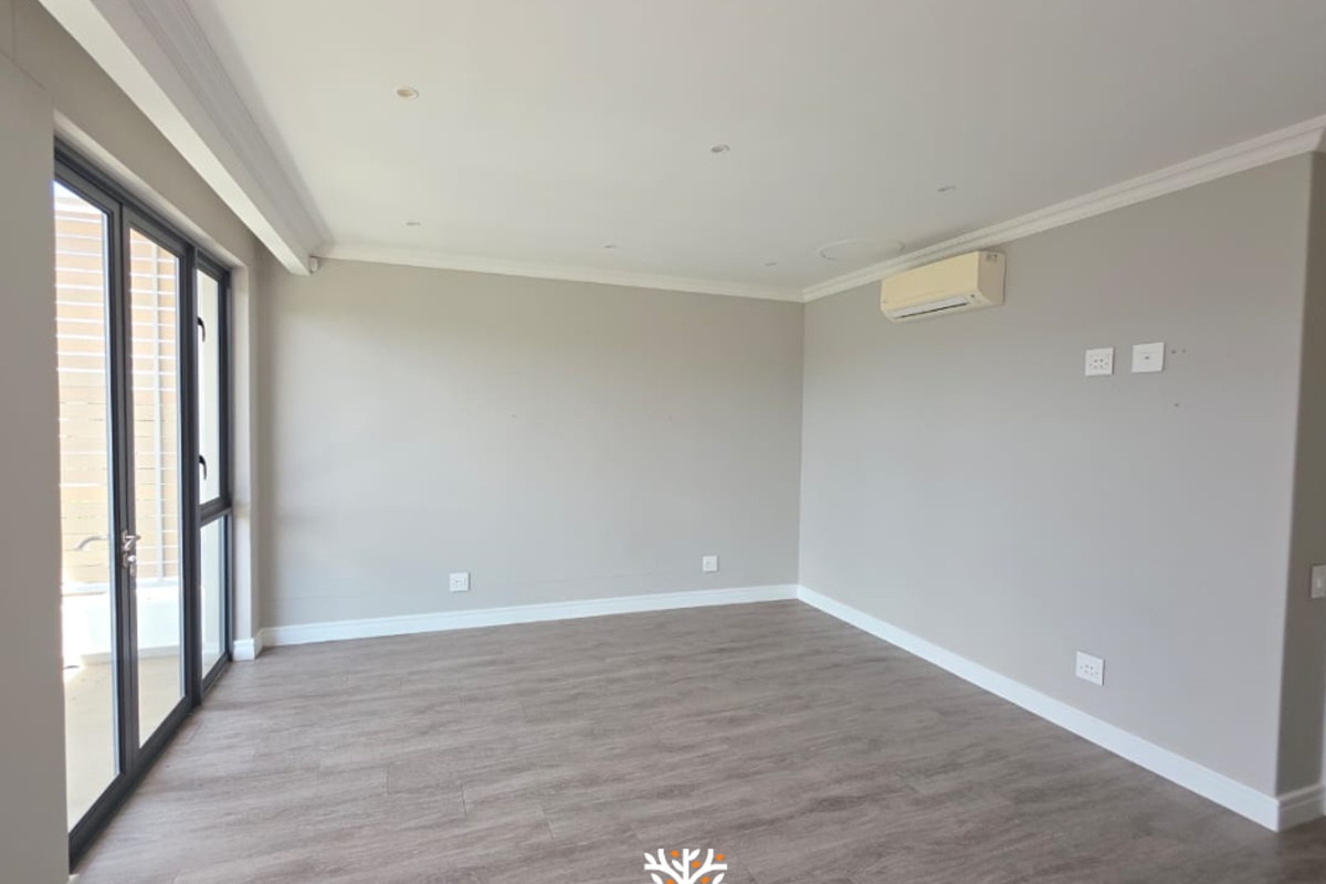A bright, empty living room featuring modern wood-look flooring, recessed ceiling lighting, a wall-mounted air conditioning unit, and large glass sliding doors.