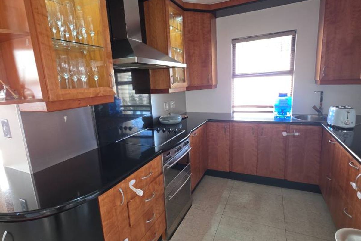 A functional kitchen featuring warm-toned wooden cabinetry, black granite countertops, stainless steel appliances, and tiled flooring with ample storage space.