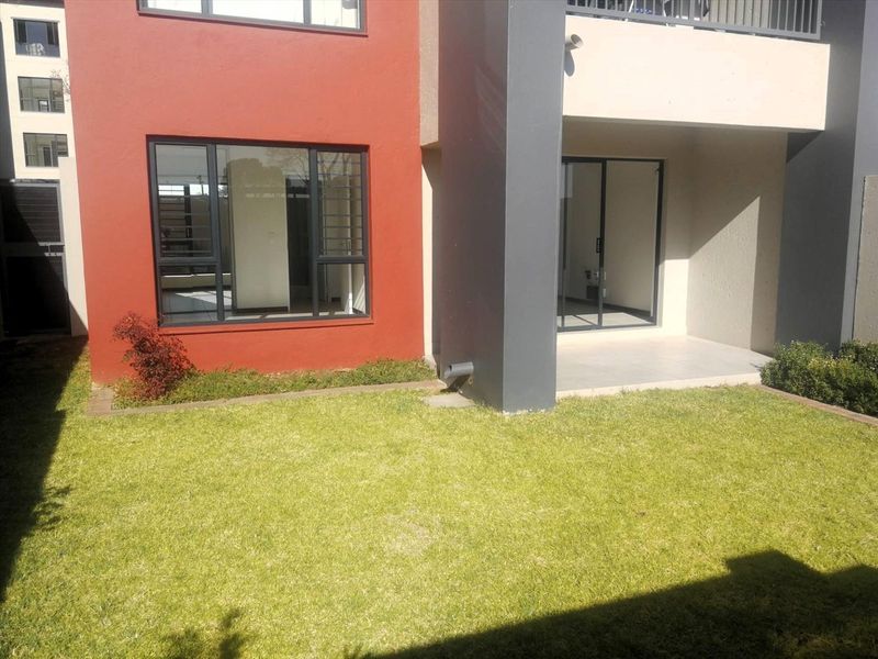 Rear view of the apartment featuring a private lawn, a covered tiled patio, and large sliding glass doors providing access to the interior living space.