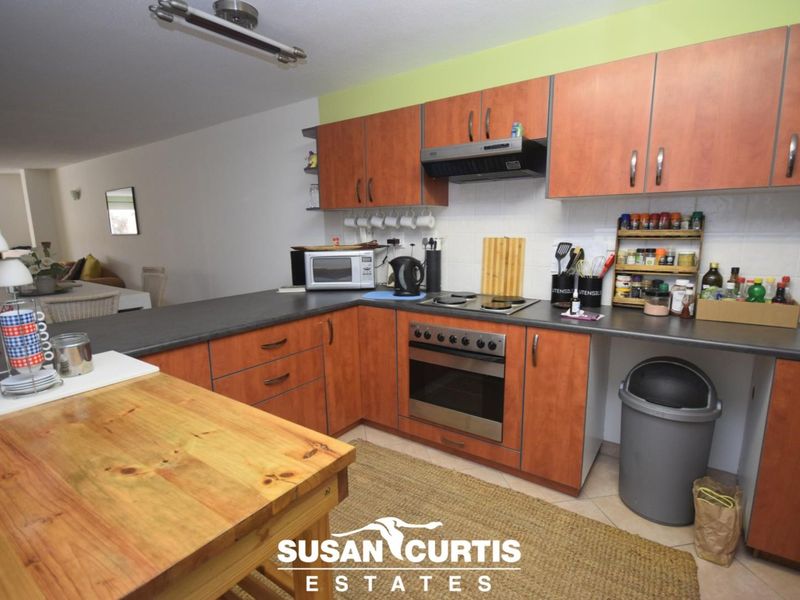 Open-plan kitchen featuring wood-look laminate cabinetry, dark countertops, built-in oven, and electric hob, seamlessly flowing into the adjacent living and dining area.