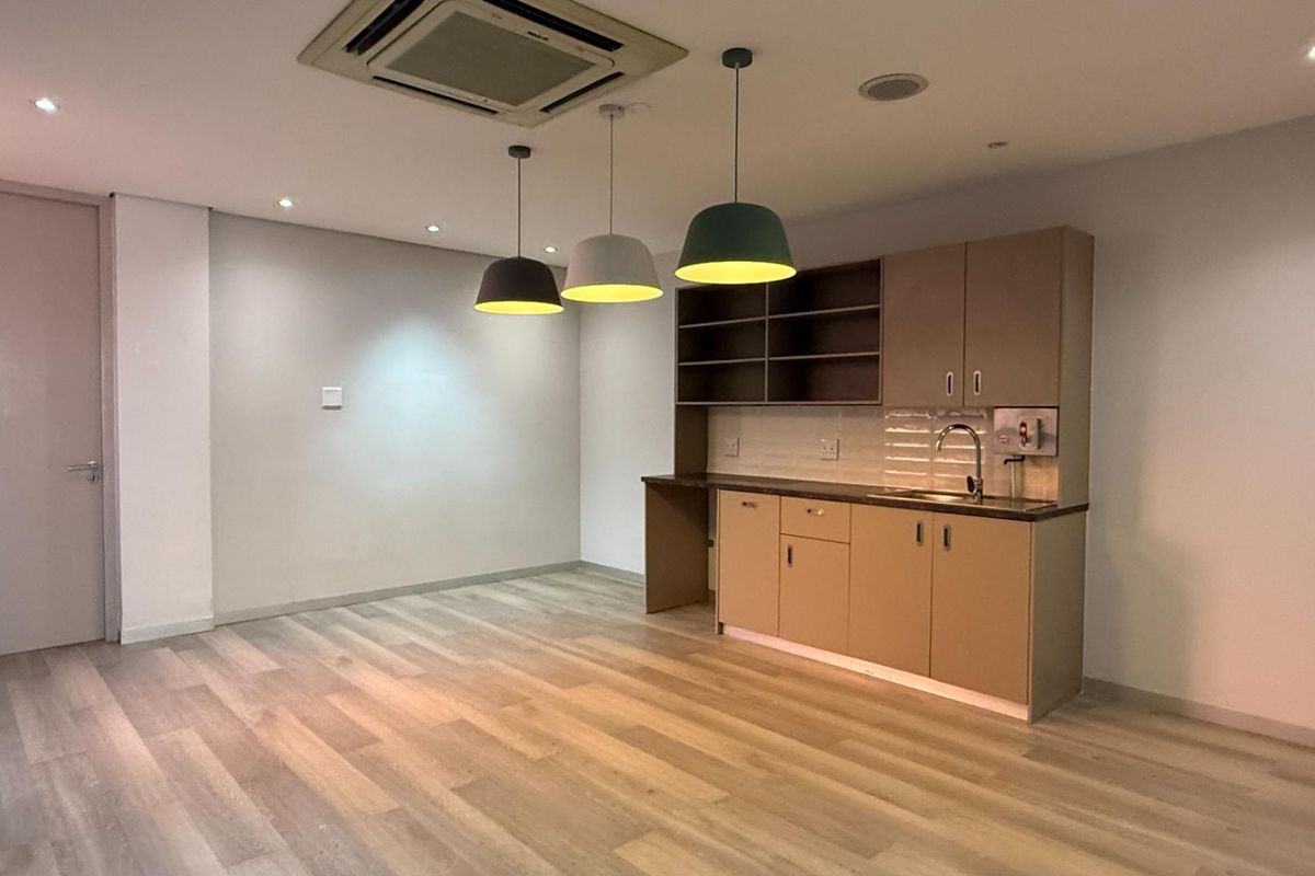 A clean, modern office kitchenette featuring built-in cabinetry, a sink, tiled backsplash, and contemporary pendant lighting, set within a bright, open-plan workspace.