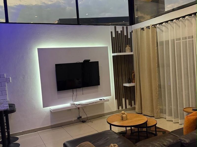 Modern living room featuring a built-in media wall with integrated LED lighting, high ceilings with clerestory windows, and polished tile flooring.
