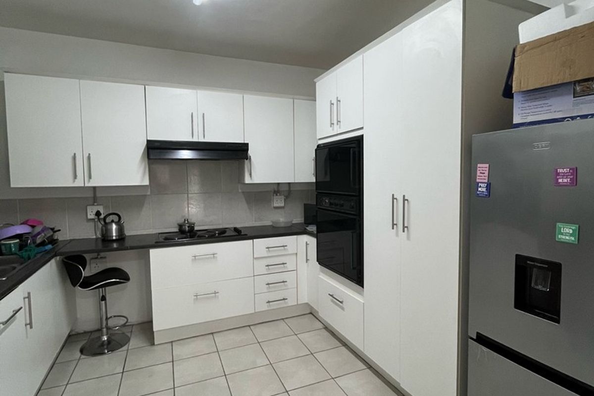 A functional kitchen featuring white built-in cabinetry, integrated oven and microwave, dark countertops, and tiled flooring with a clean, modern layout.