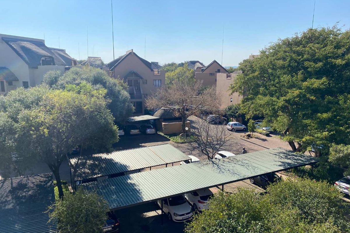 Elevated view of the apartment complex grounds, featuring paved parking areas with covered carports and established trees.