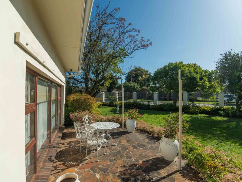 A paved outdoor patio area adjacent to the house, featuring sliding glass doors and access to a well-maintained garden.