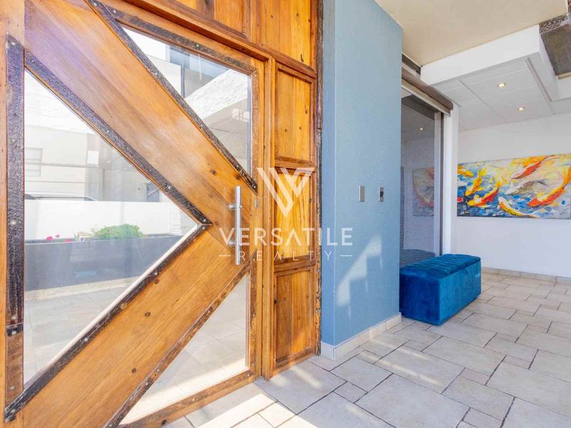 A bright and welcoming entrance hall featuring a large timber-framed glass door and neutral tiled flooring.