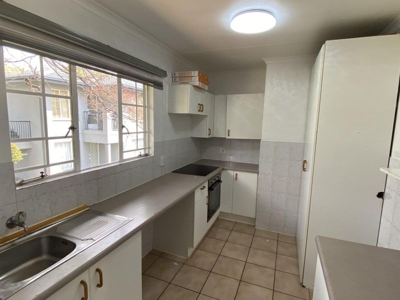 A functional kitchen featuring built-in cabinetry, laminate countertops, a stainless steel sink, and integrated oven and hob, with tiled flooring and splashbacks.