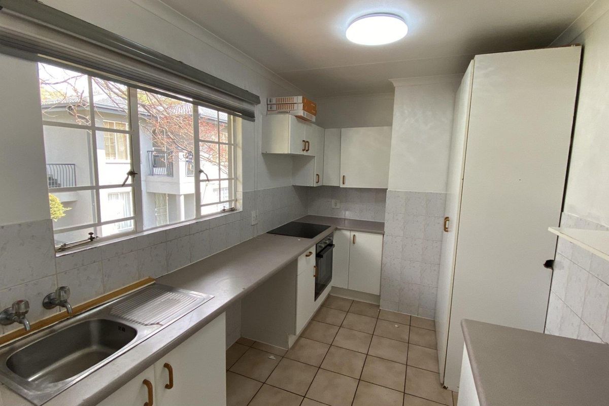 A functional kitchen featuring built-in cabinetry, laminate countertops, a stainless steel sink, and integrated oven and hob, with tiled flooring and splashbacks.
