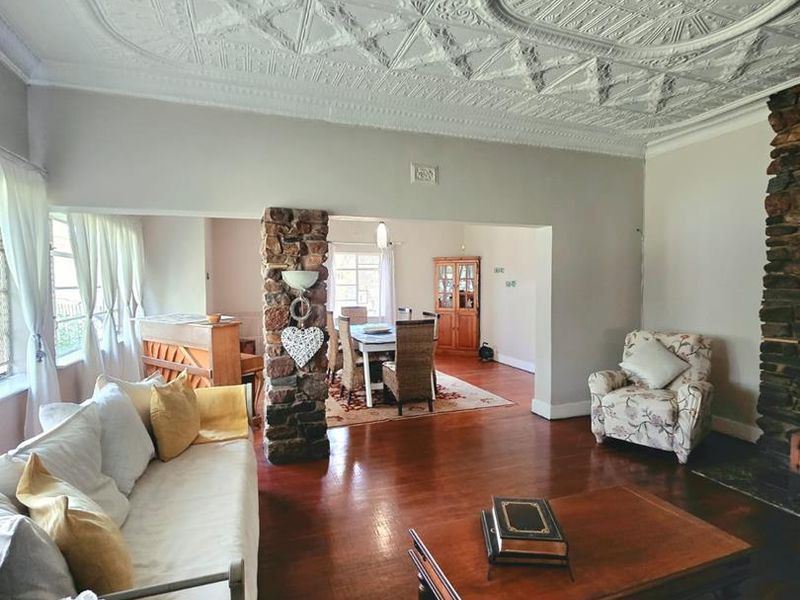 Spacious open-plan living and dining area featuring a striking ornate pressed metal ceiling, hardwood flooring, and a characterful stone fireplace.