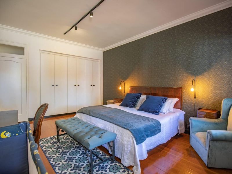 Spacious bedroom featuring hardwood flooring, a decorative wallpaper accent wall, built-in storage cupboards, and modern track lighting.