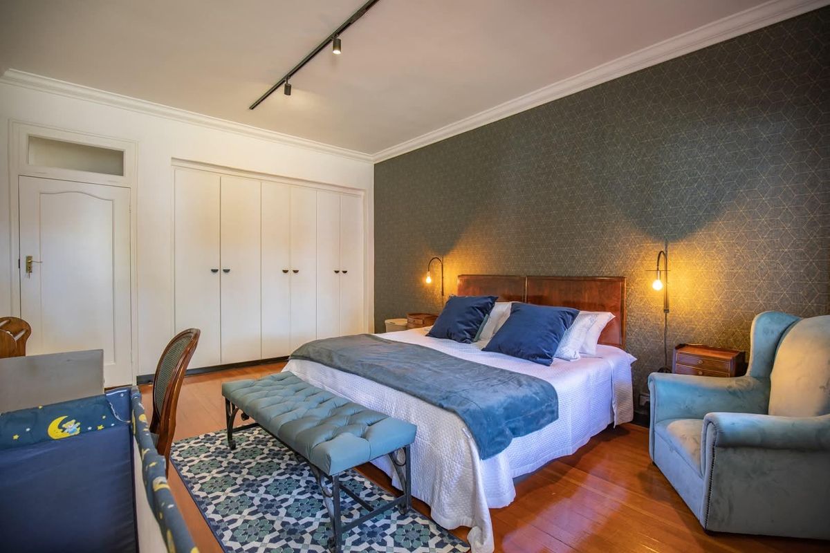 Spacious bedroom featuring hardwood flooring, a decorative wallpaper accent wall, built-in storage cupboards, and modern track lighting.