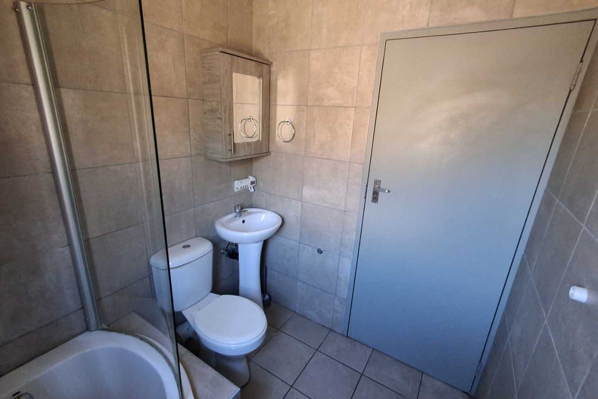 A functional bathroom featuring a glass-enclosed shower, pedestal basin, and toilet, finished with neutral wall and floor tiling.