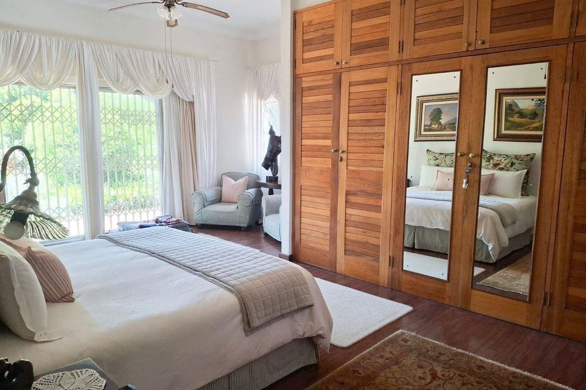 Spacious bedroom featuring extensive built-in wooden cabinetry with integrated mirrors, ceiling fan, and large sliding glass doors with security gates leading outdoors.