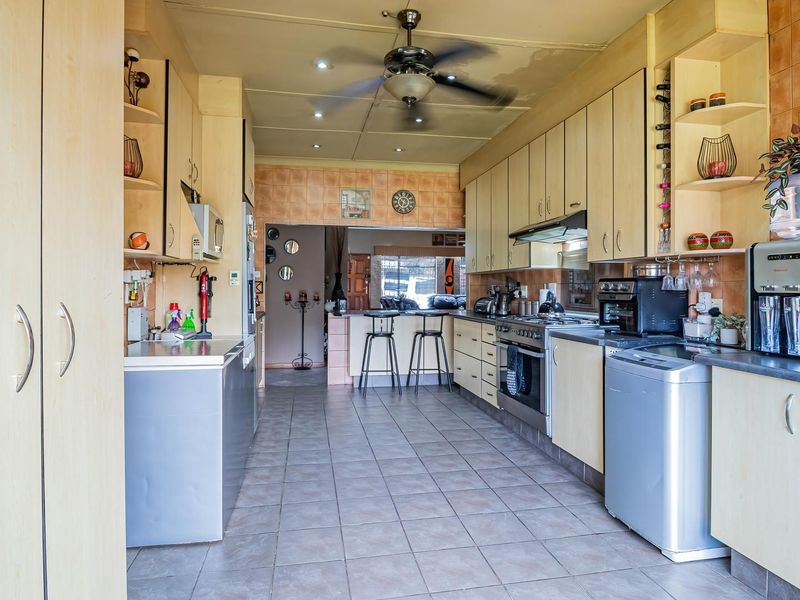 A functional kitchen featuring light wood cabinetry, tiled flooring, a gas stove with extractor fan, and a breakfast counter leading to the living area.