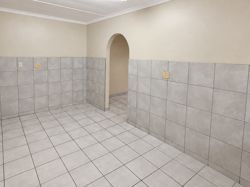 An empty utility space featuring neutral half-height wall tiling, tiled floors, and an arched entryway, providing a clean and functional area.