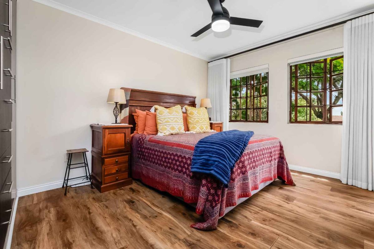 A well-maintained bedroom featuring wood-look flooring, built-in cabinetry, a ceiling fan, and large windows that provide natural light and garden views.