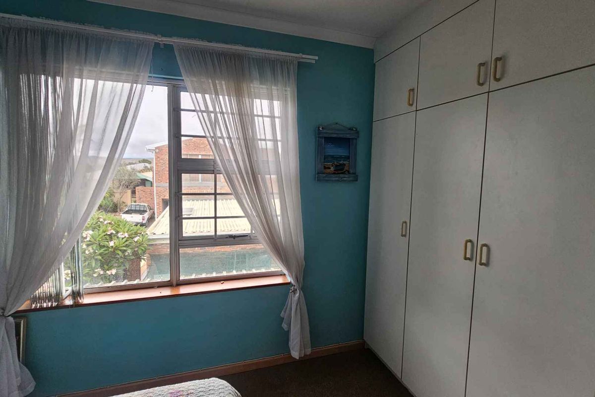 A bedroom featuring built-in floor-to-ceiling wardrobes, a large window with security bars, and blue painted walls.