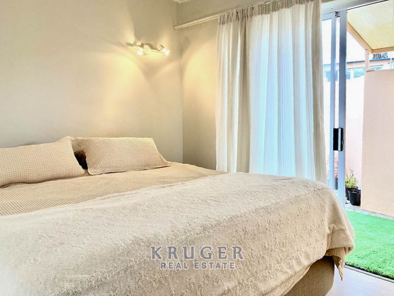 A bright bedroom featuring a sliding glass door that opens to an outdoor patio area, complemented by neutral wall tones and modern lighting.
