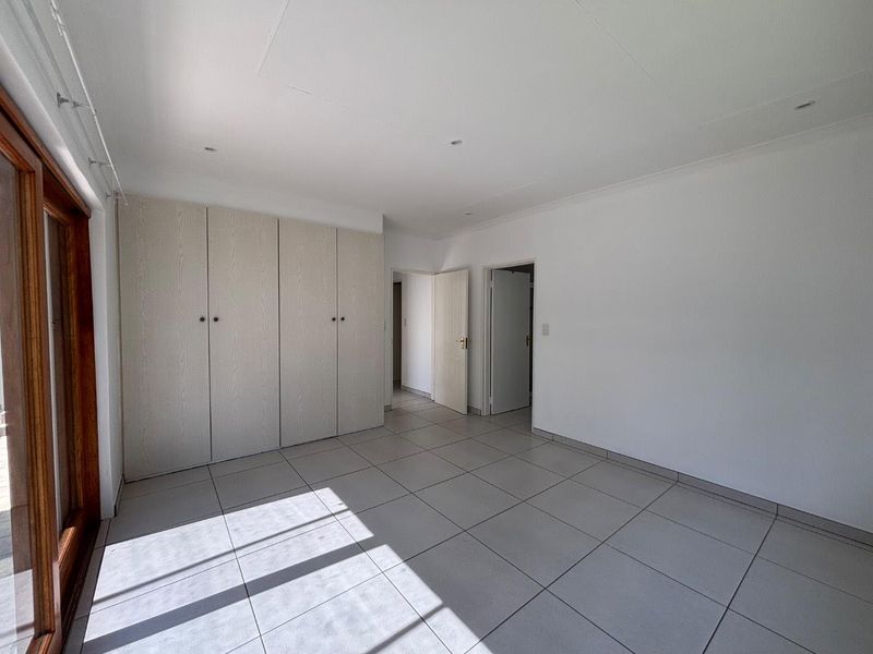 A bright, empty bedroom featuring neutral tiled flooring, built-in cupboards, and a sliding glass door providing natural light.