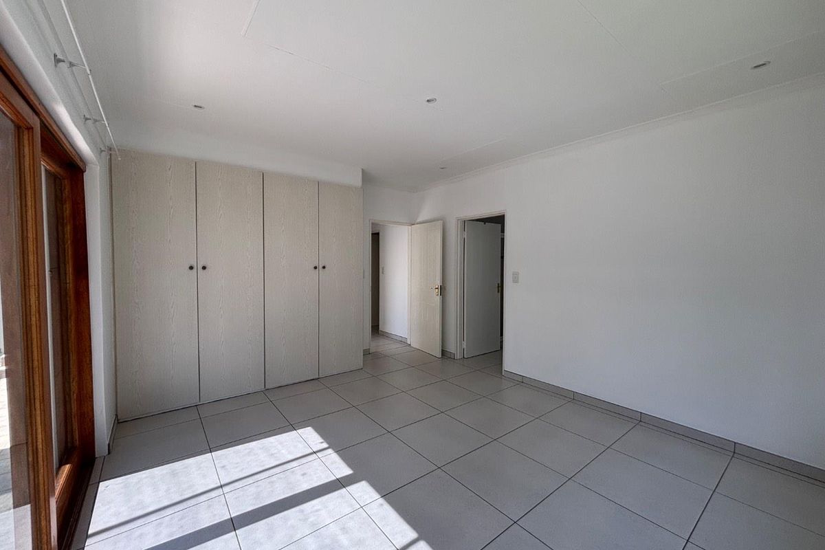 A bright, empty bedroom featuring neutral tiled flooring, built-in cupboards, and a sliding glass door providing natural light.