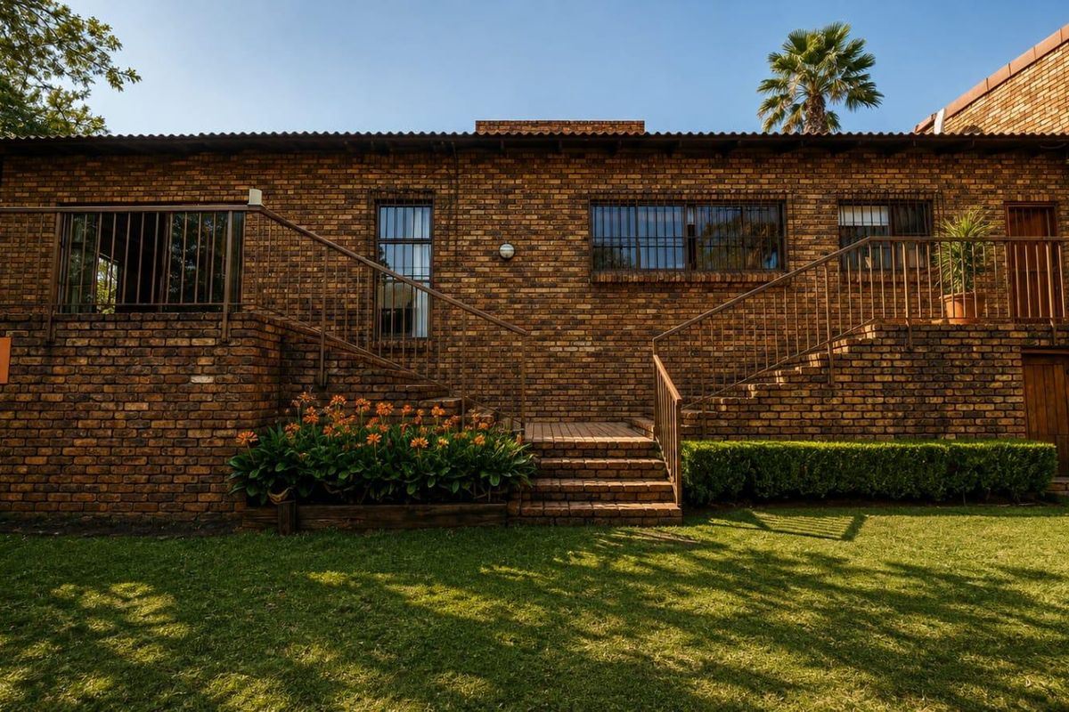 Rear view of a face brick house featuring a raised patio area, metal security railings, and a staircase leading to the garden.