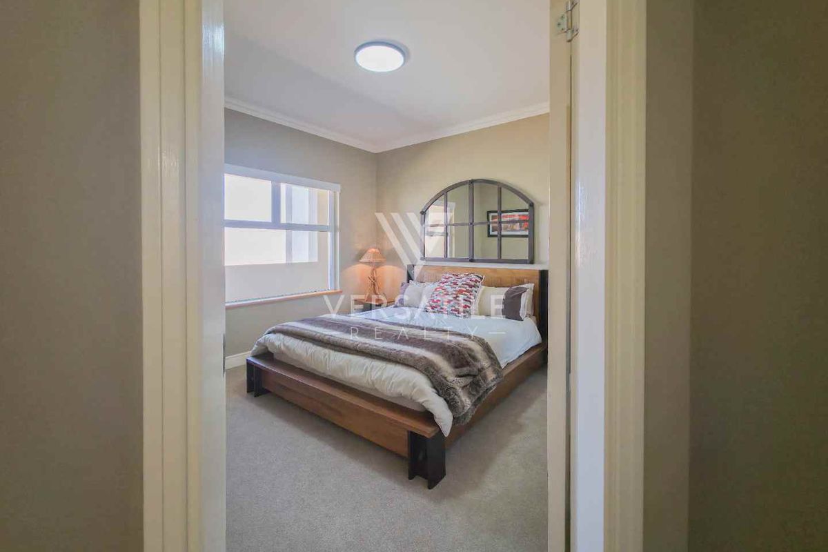 A view into a carpeted bedroom featuring a window and a central ceiling light fixture, viewed from the adjacent hallway.