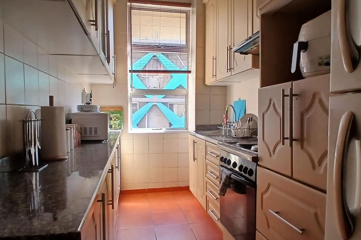 A functional galley-style kitchen featuring granite countertops, ample built-in cabinetry, a tiled backsplash, and a freestanding oven with an extractor fan.