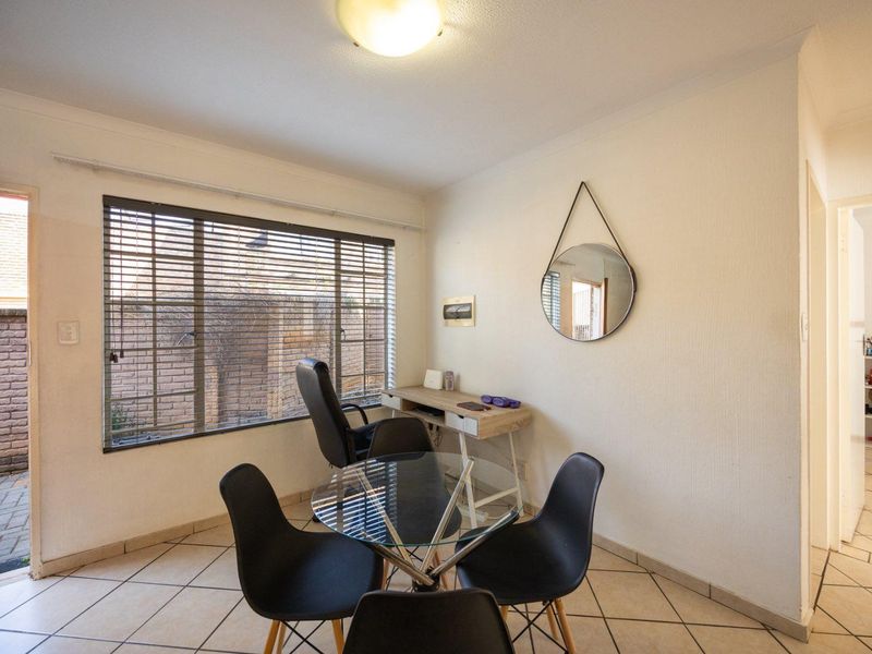 A functional dining area featuring tiled flooring, a large window with venetian blinds, and direct access to an outdoor space.