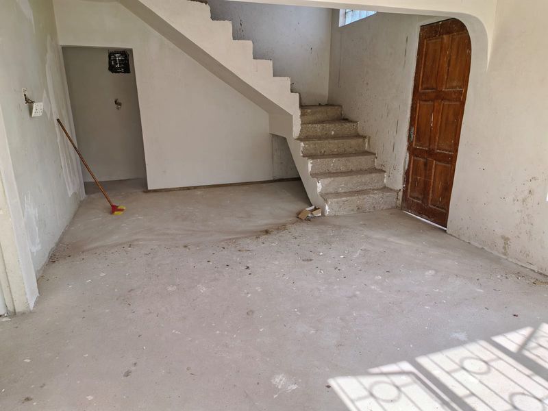 An unfinished interior space featuring a concrete staircase, wooden door, and raw wall surfaces, offering a blank canvas for renovation and interior design.