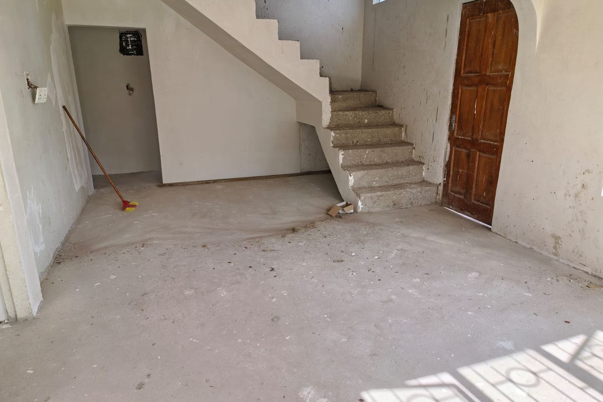 An unfinished interior space featuring a concrete staircase, wooden door, and raw wall surfaces, offering a blank canvas for renovation and interior design.
