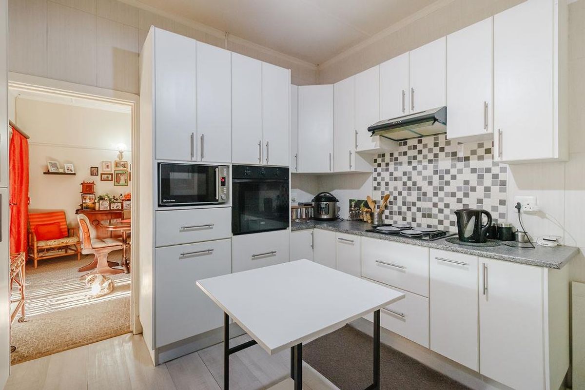 A functional kitchen featuring white cabinetry, a built-in oven and microwave, gas hob with extractor fan, and a modern tiled backsplash.