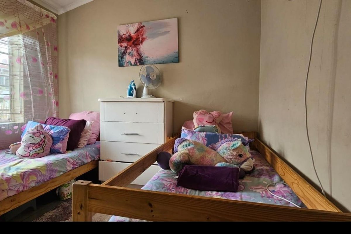 A functional bedroom featuring a large window with security bars, neutral wall finishes, and space for multiple beds.