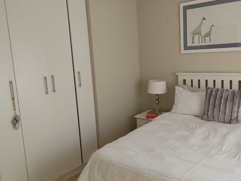 A well-maintained bedroom featuring neutral wall tones, tiled flooring, and a functional built-in wardrobe with modern hardware.