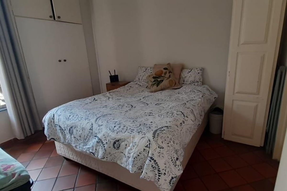 A functional bedroom featuring built-in cupboards, tiled flooring, and security bars on the window, providing a practical and secure living space.