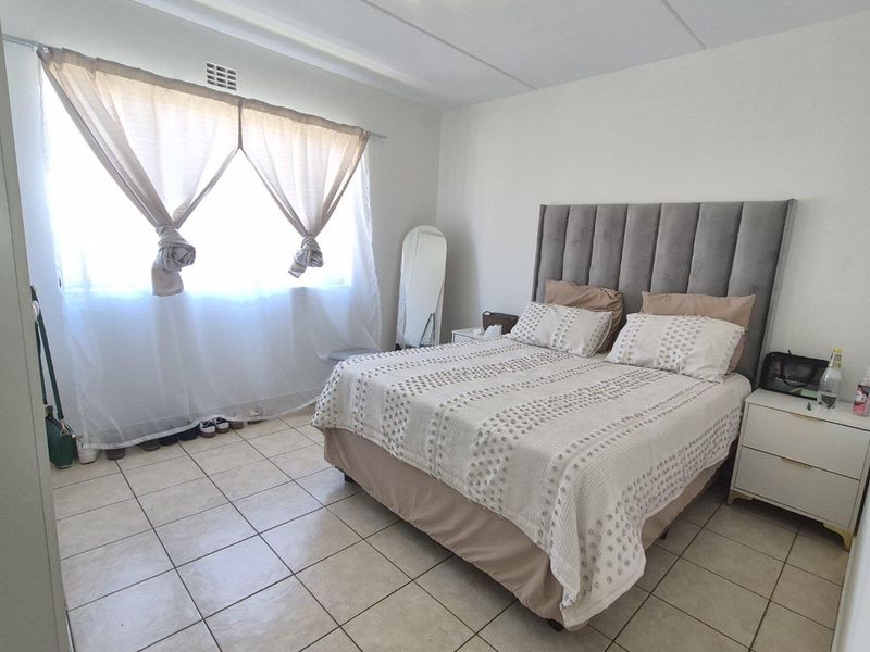 A well-lit bedroom featuring neutral tiled flooring and a functional ventilation grille, offering a clean and simple space.
